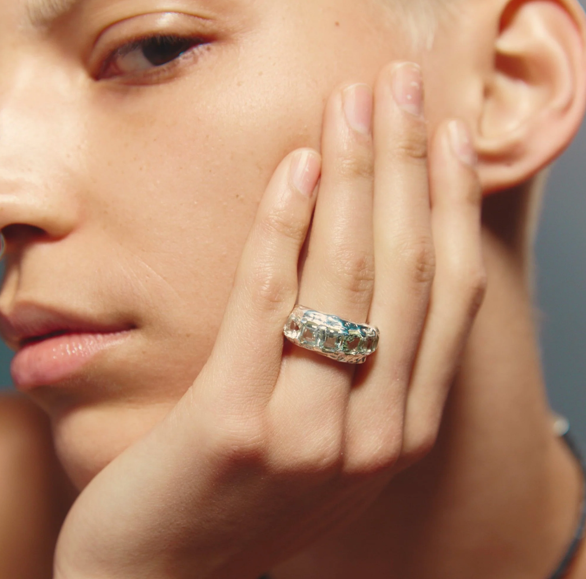 Close-up of a person wearing a diamond ring on a neutral background