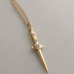 Gold dagger-shaped necklace with embedded stones on a light gray background
