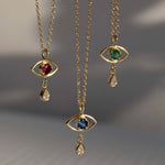 Three gold necklaces with eye-shaped pendants featuring gemstones on a gray background.