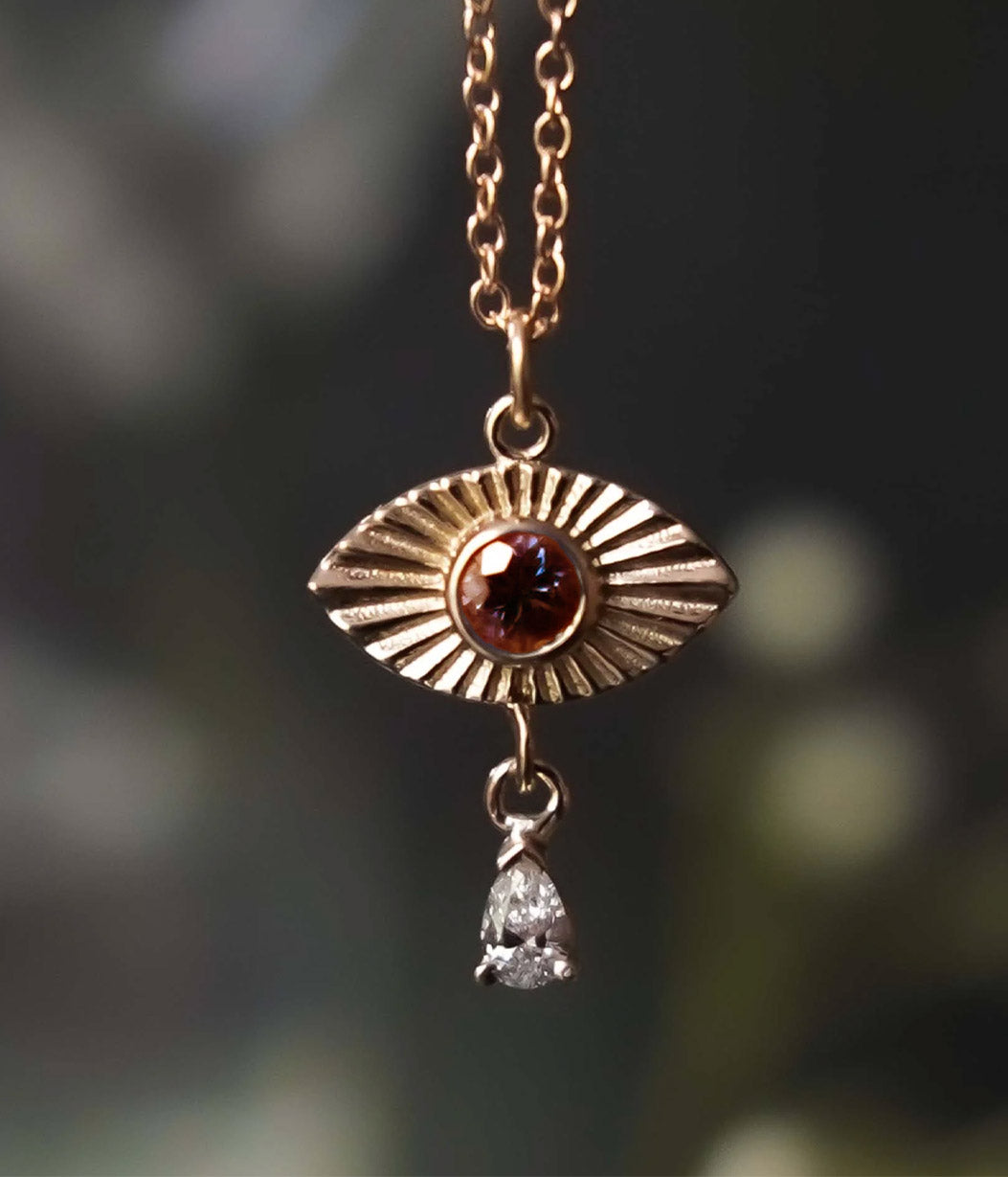 Gold pendant with blue gemstone and diamond drop against a blurred natural background