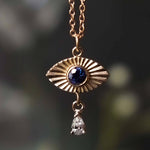 Gold pendant with blue gemstone and diamond drop against a blurred natural background