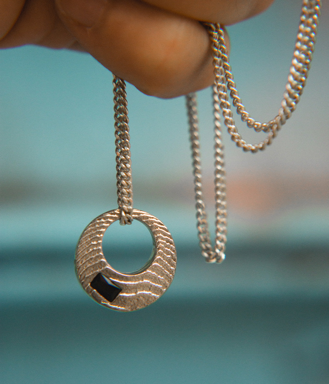 Silver necklace with a textured pendant held against a blurred natural background