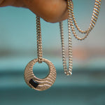 Silver necklace with a textured pendant held against a blurred natural background