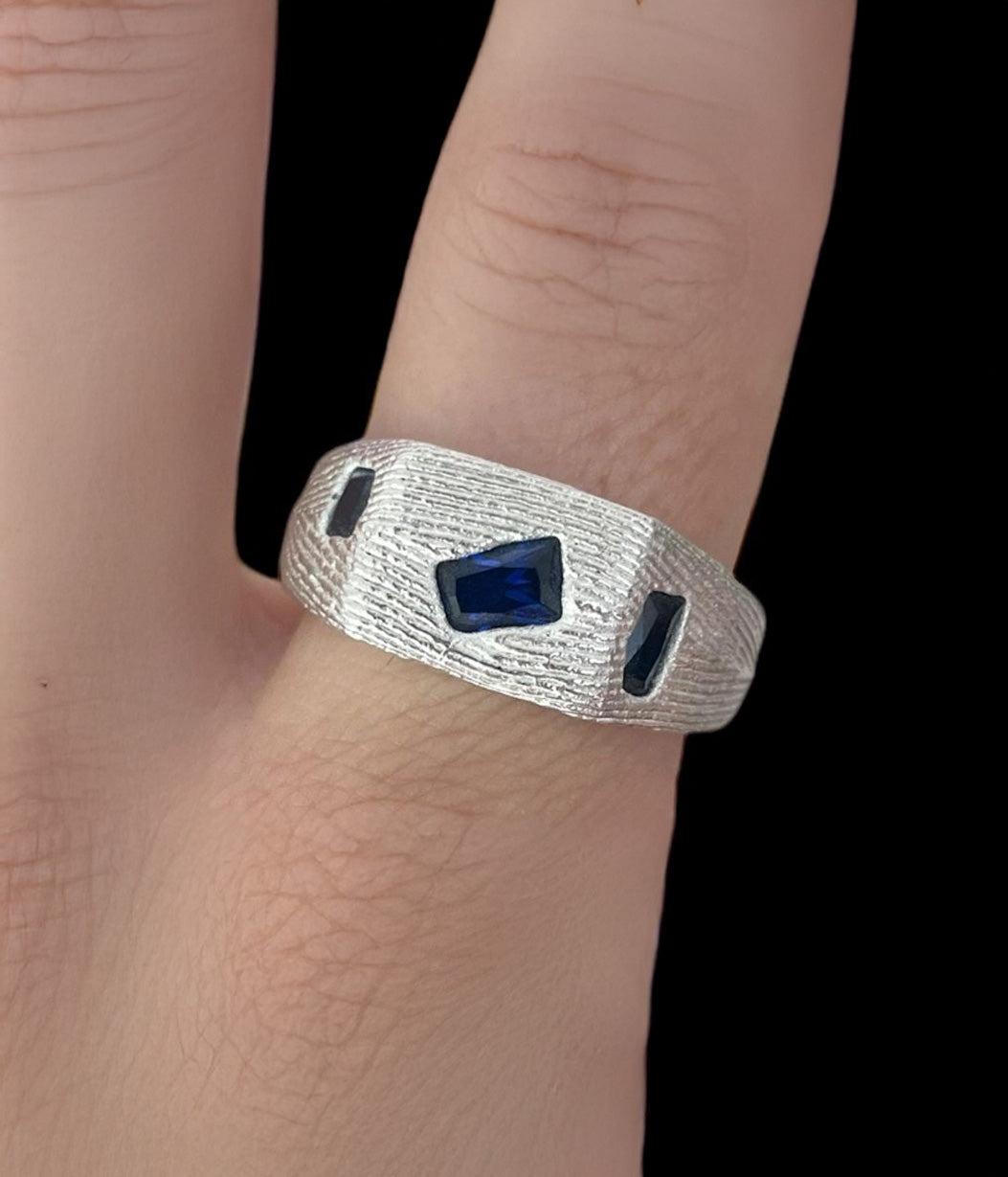 Silver ring with blue gemstones on a person's finger against a black background