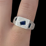 Silver ring with blue gemstones on a person's finger against a black background
