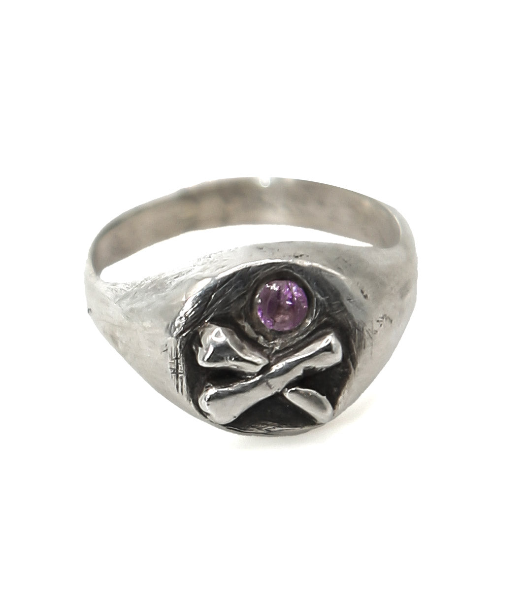 Silver ring with skull and crossbones design and purple gemstone on a white background