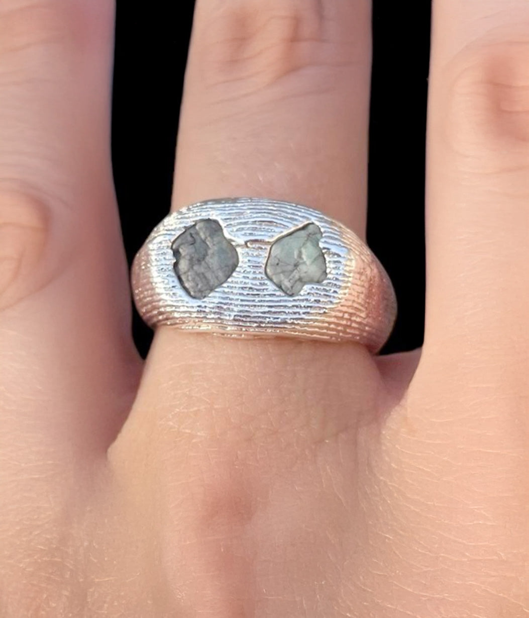 Silver ring with embedded stones on a finger against a black background