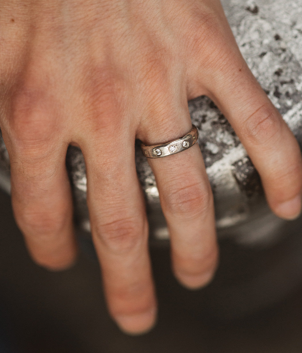 Close-up of a hand wearing a silver ring with small stones on a blurred background