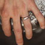 Close-up of a hand wearing a silver ring with small stones on a blurred background