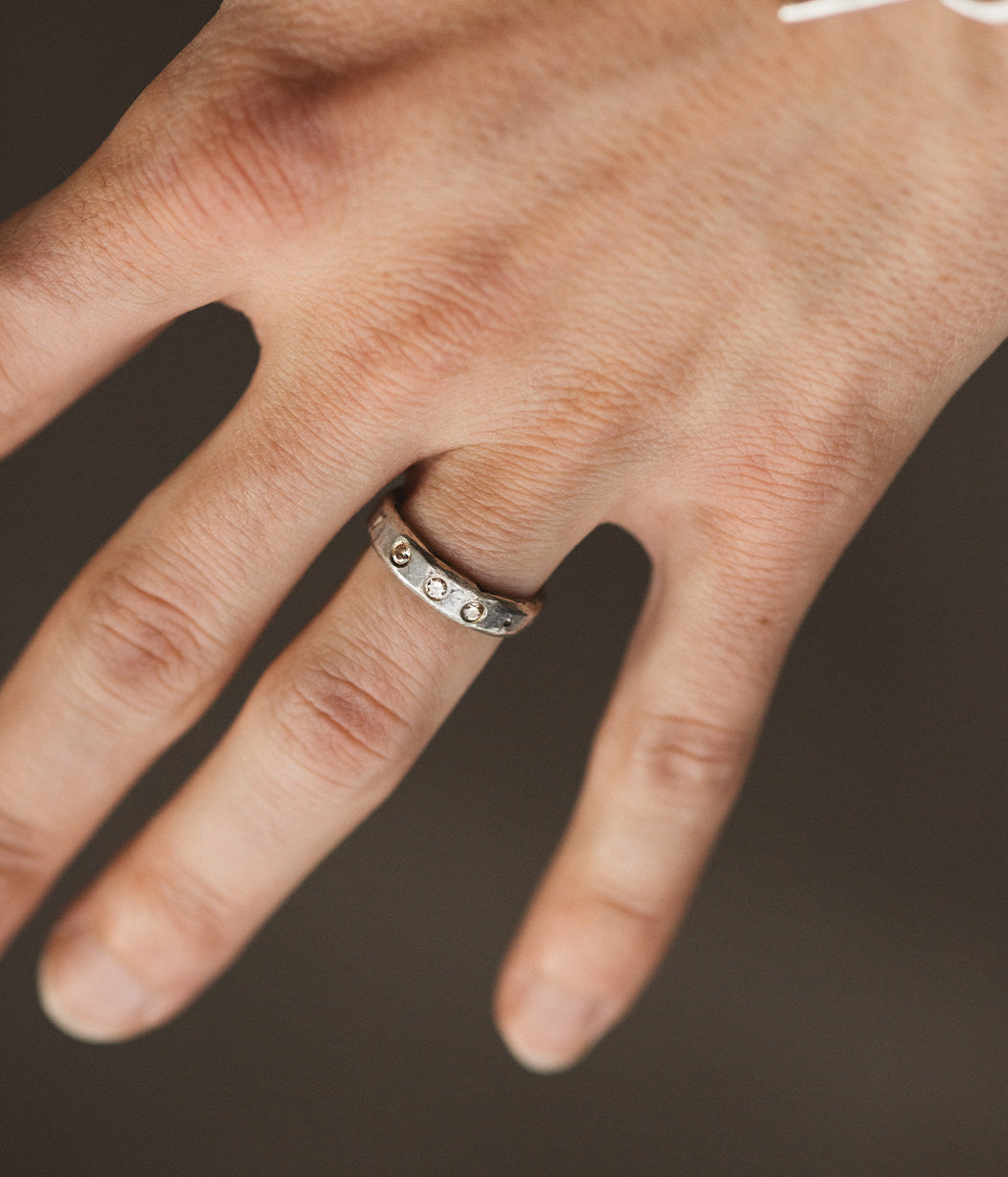 Close-up of a hand wearing a silver ring with engraved details on a dark background