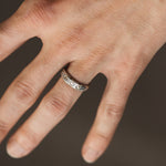 Close-up of a hand wearing a silver ring with engraved details on a dark background