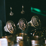 Close-up of gold rings with engraved faces on a reflective surface.