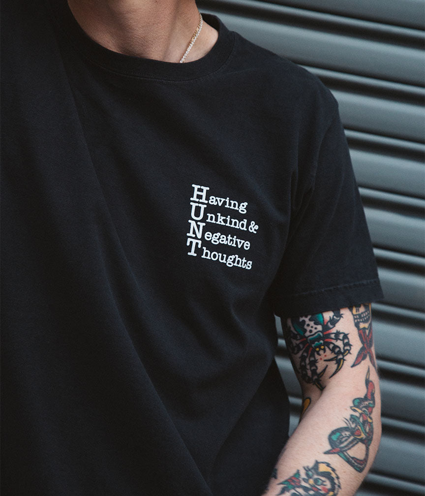 Person wearing a black t-shirt with white text, standing against a neutral background.