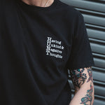 Person wearing a black t-shirt with white text, standing against a neutral background.