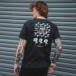 Person wearing a black t-shirt with white graphics and text, standing in front of a metallic shutter.