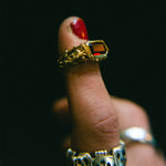 Gold ring with a red gemstone on a finger against a dark background