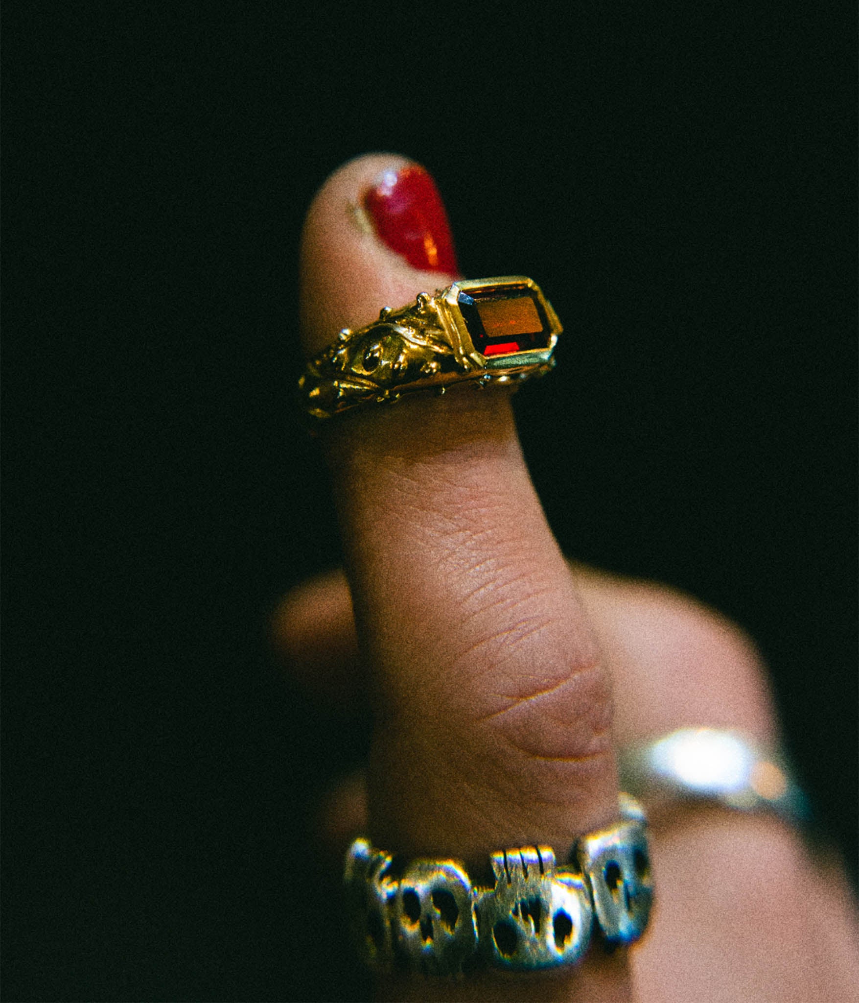 Gold ring with a red gemstone on a finger against a dark background