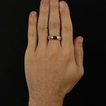 Hand wearing a ring with a red stone on a black background