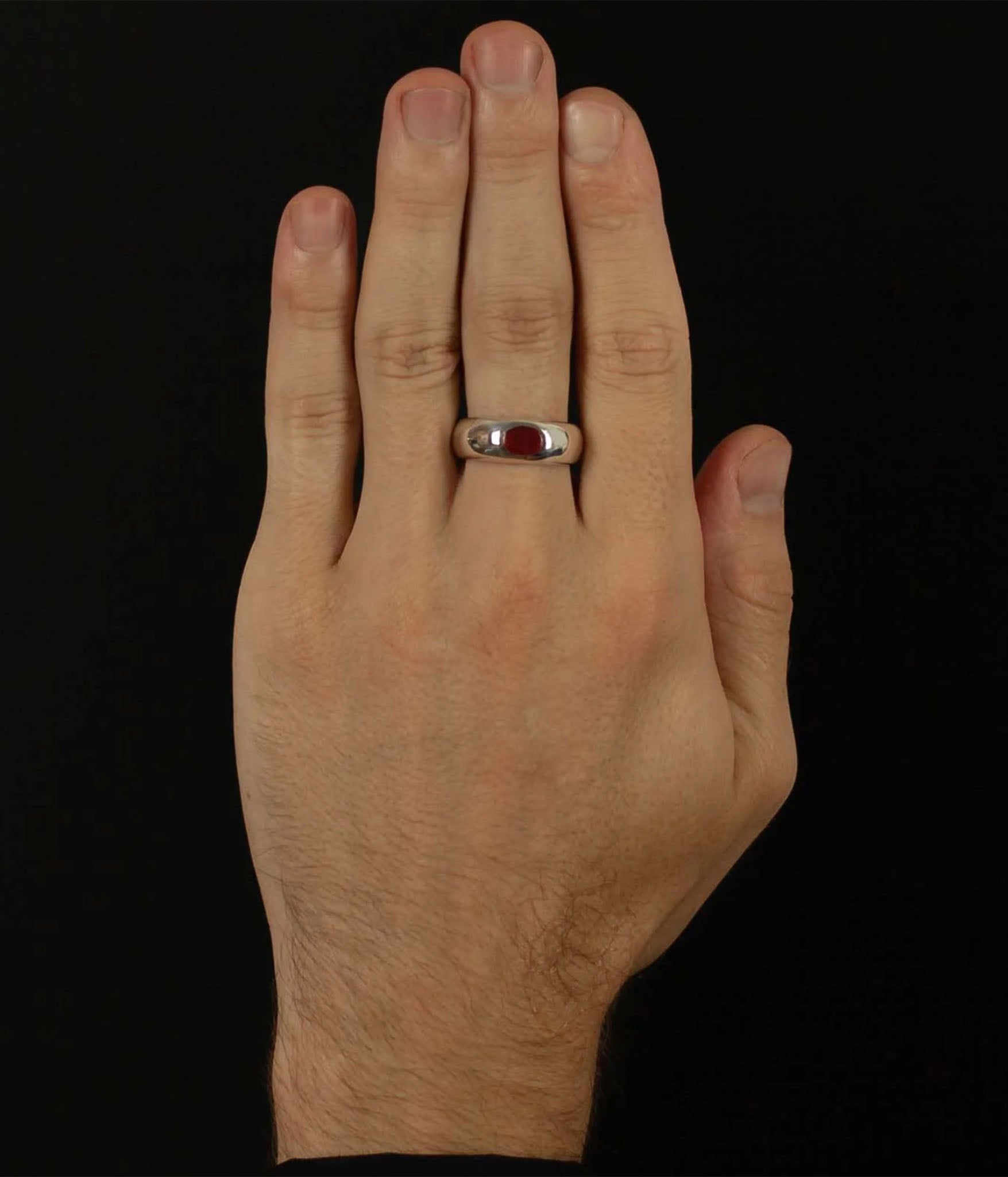 Hand wearing a ring with a red stone on a black background