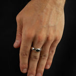Hand wearing a silver ring on a black background