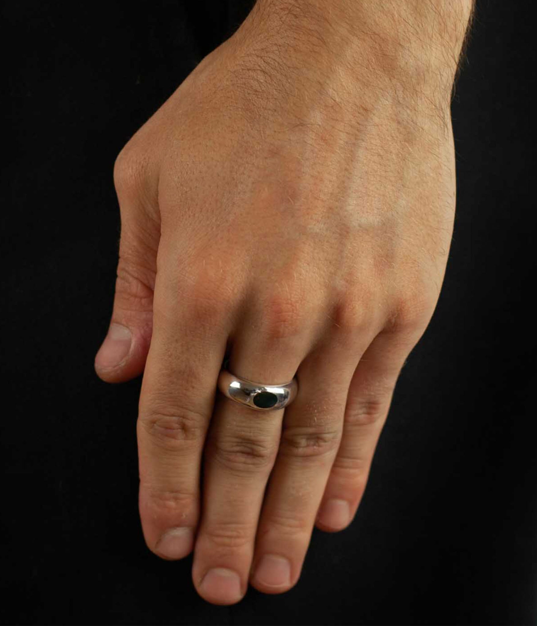 Hand wearing a silver ring on a black background