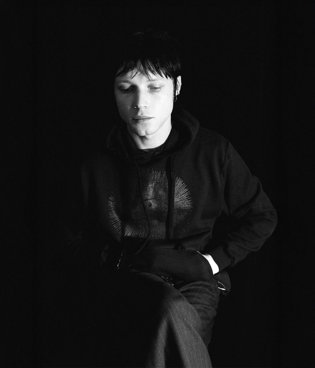 Person wearing a dark hoodie with a logo on a black background