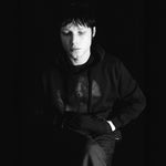 Person wearing a dark hoodie with a logo on a black background