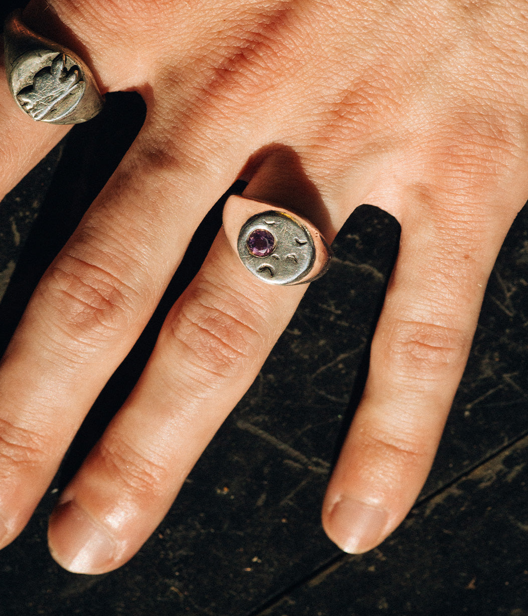 Close-up of a hand wearing a silver ring with a purple gemstone on a dark surface.