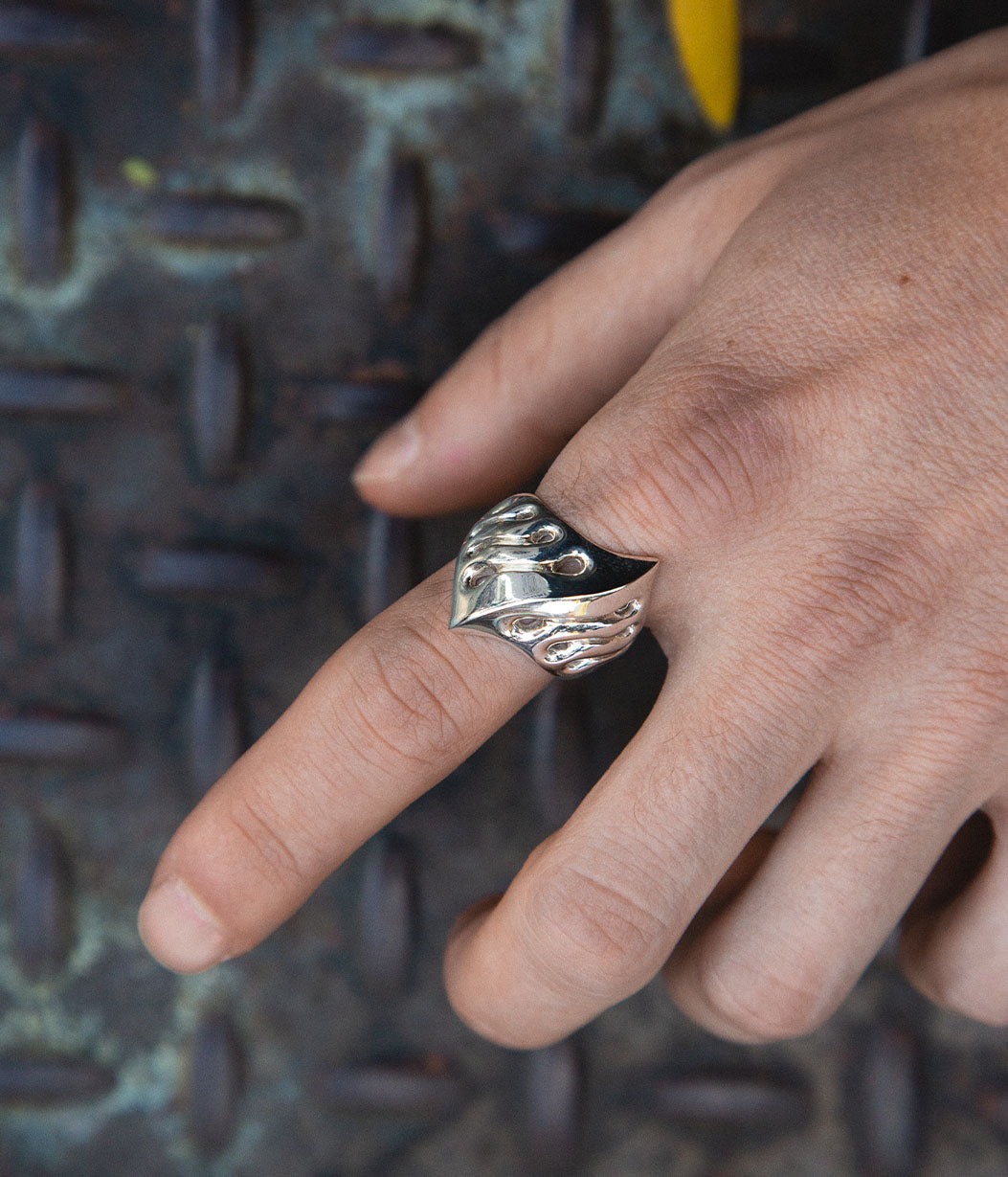 Hand wearing a silver paw print ring on a textured metal surface