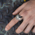 Hand wearing a silver paw print ring on a textured metal surface