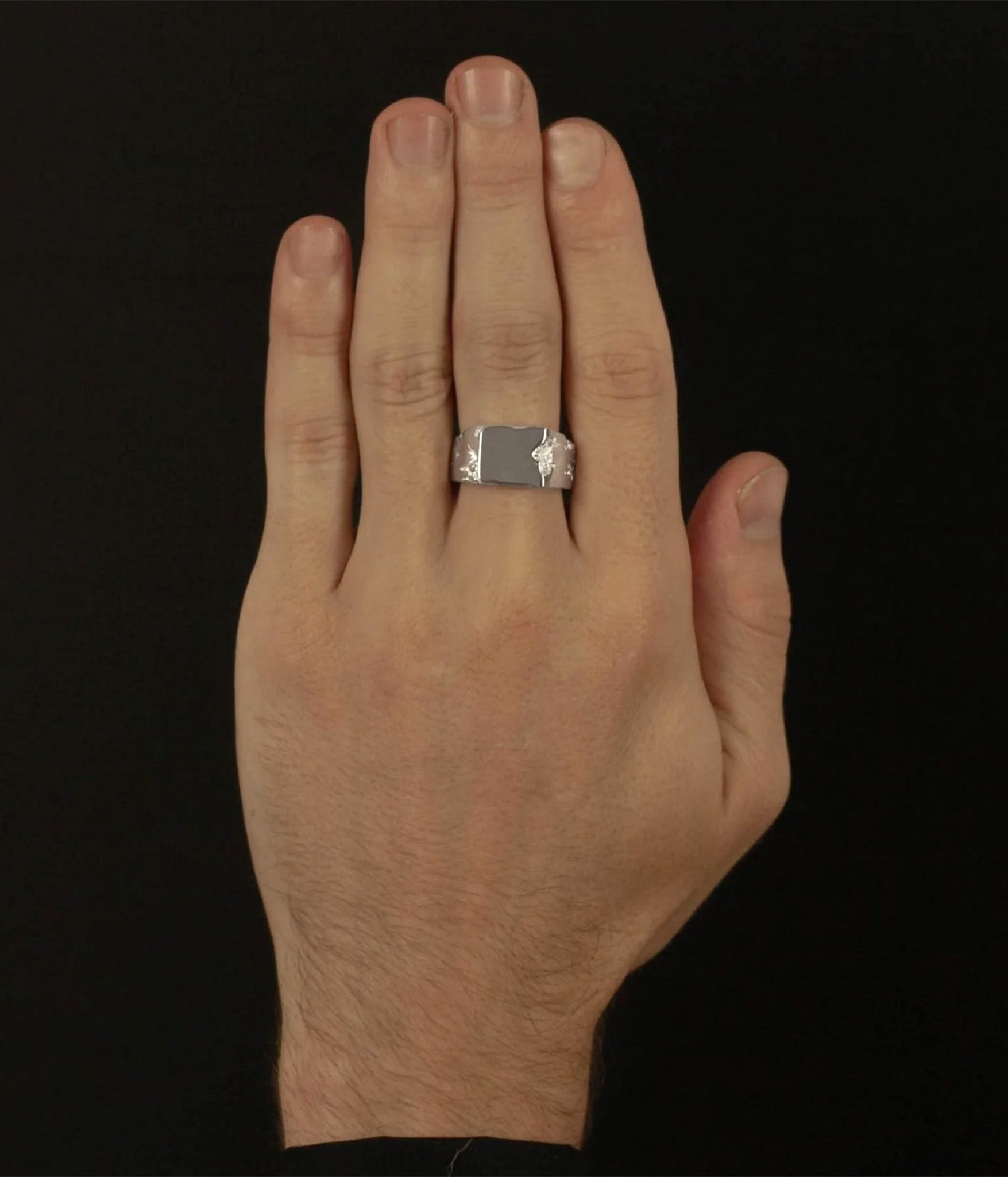 Hand wearing a silver ring on a black background