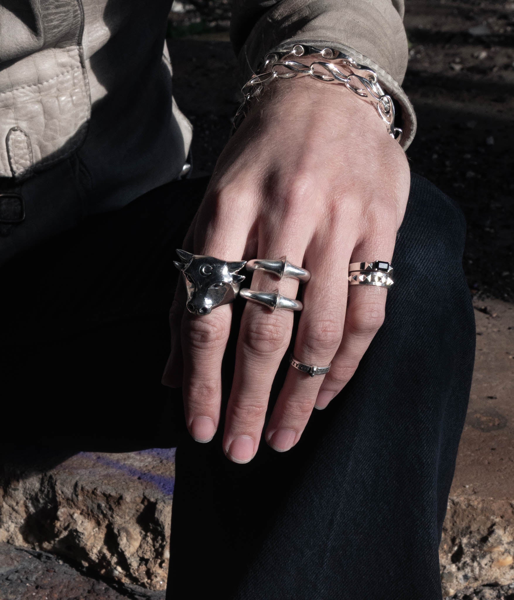 Close-up of a hand wearing multiple silver rings with a dark background
