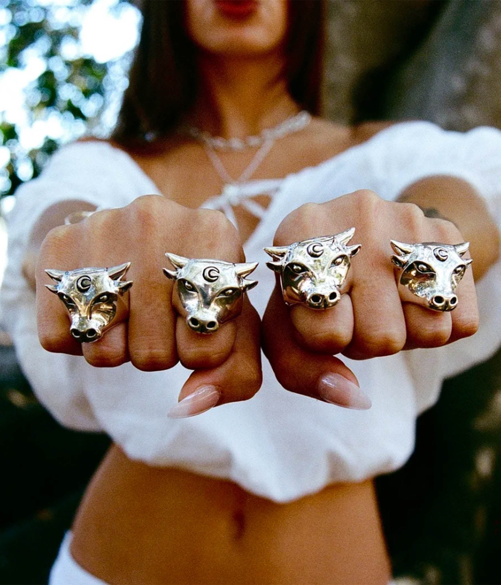 Four gold rings with bull head designs on a person's fingers outdoors.
