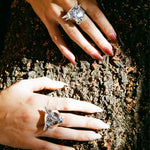 Two hands wearing silver rings with cat designs on a textured surface.