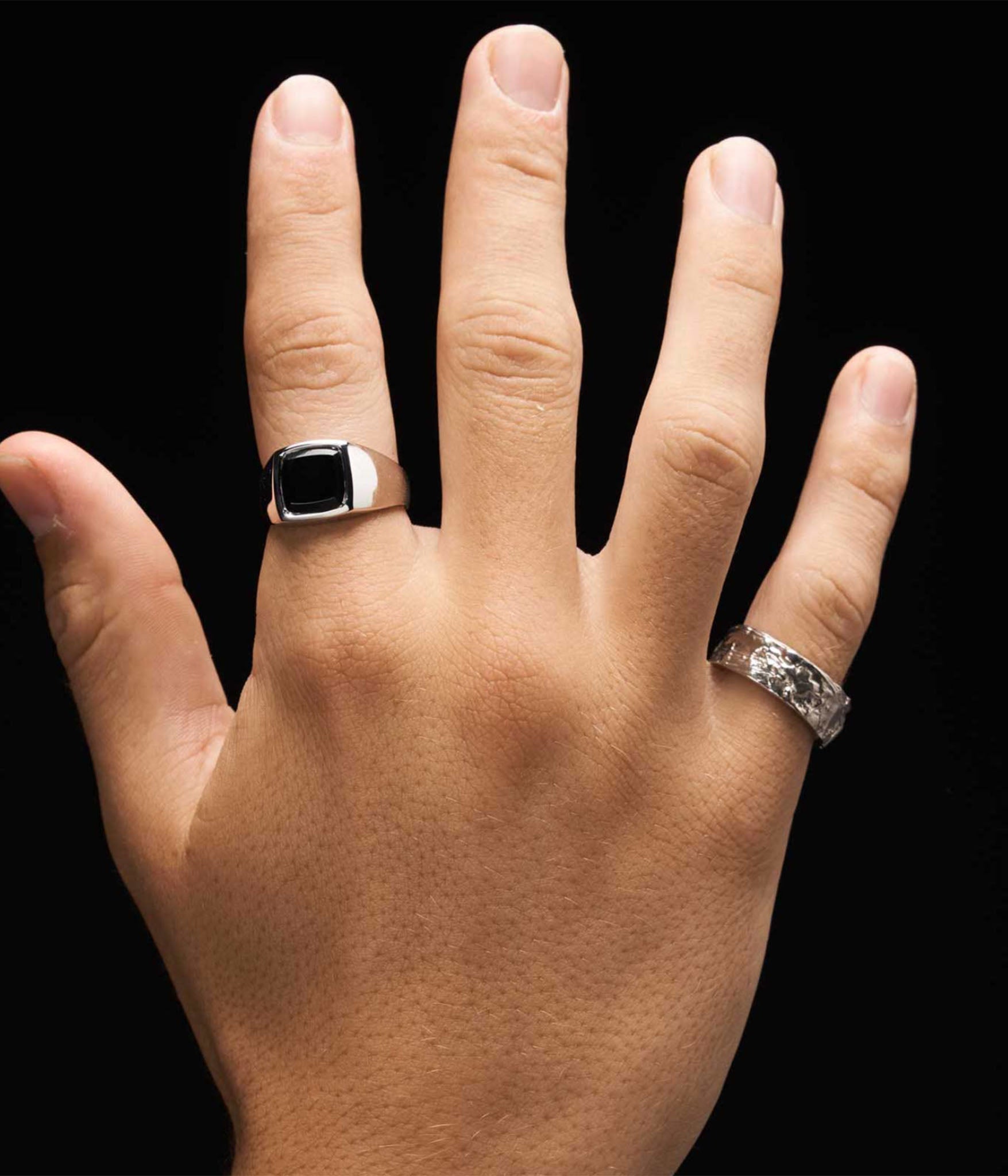 Hand wearing two rings on a black background