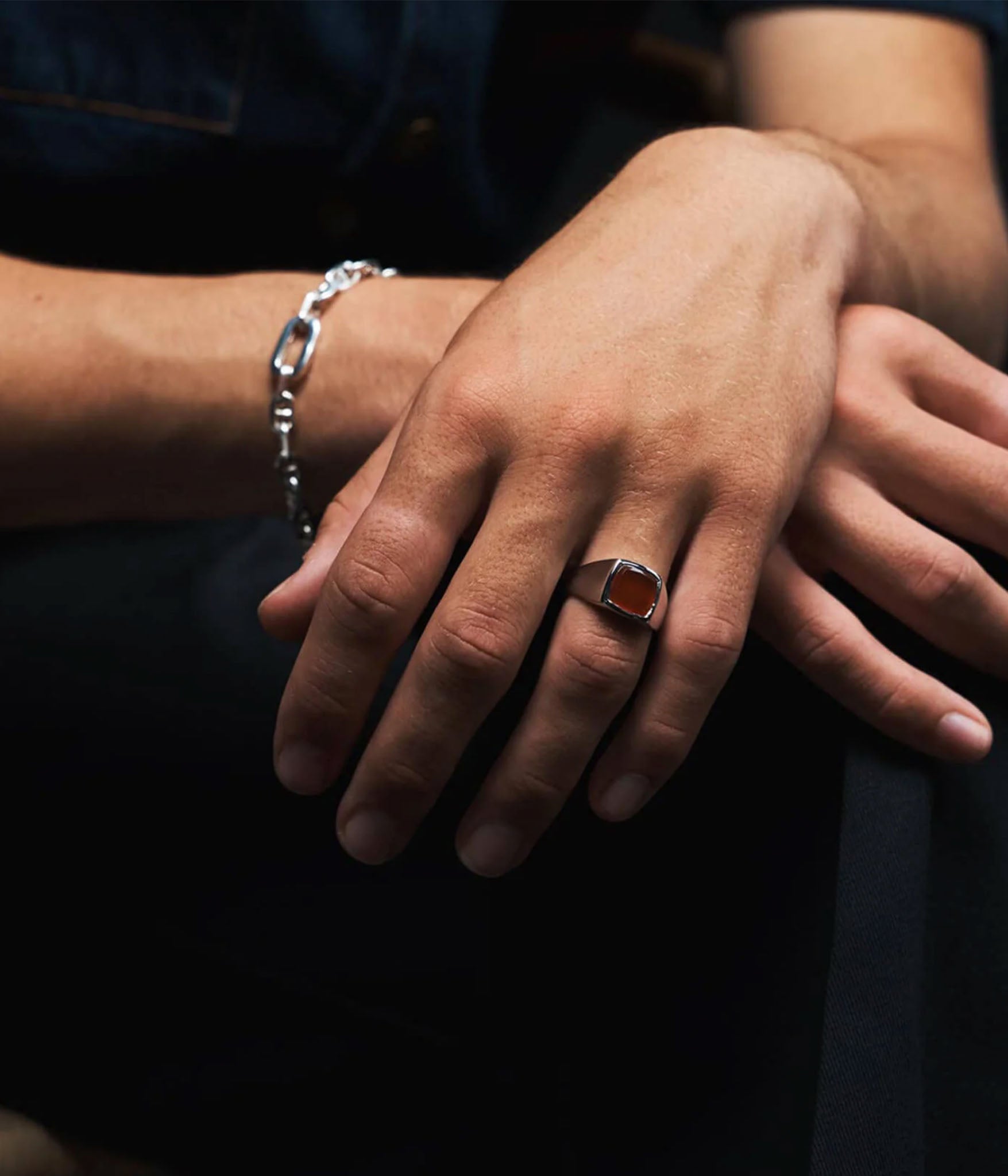 Close-up of hands with a ring and bracelet on a dark background