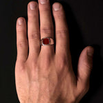 Hand wearing a ring with a red stone on a black background