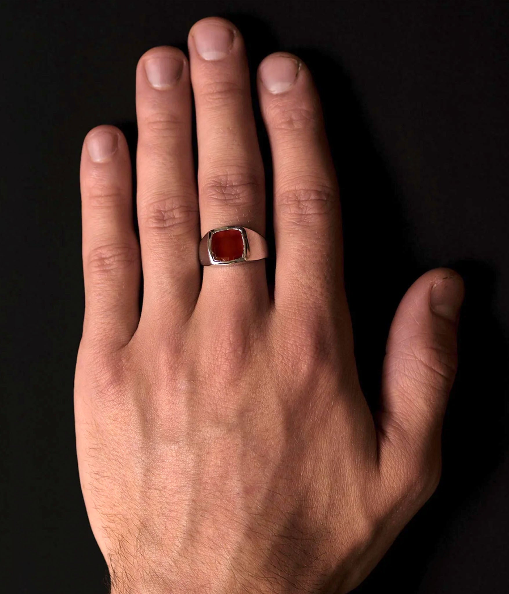 Hand wearing a ring with a red stone on a black background