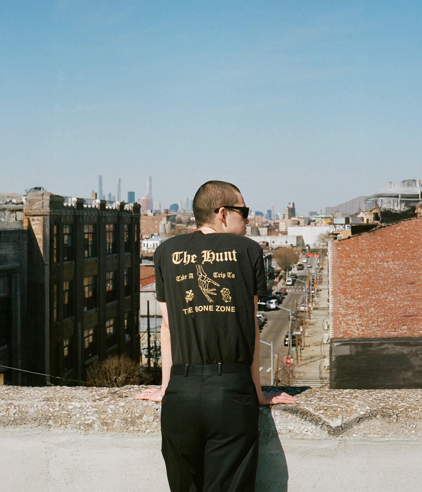 Person wearing a black t-shirt with text on a rooftop with cityscape in the background