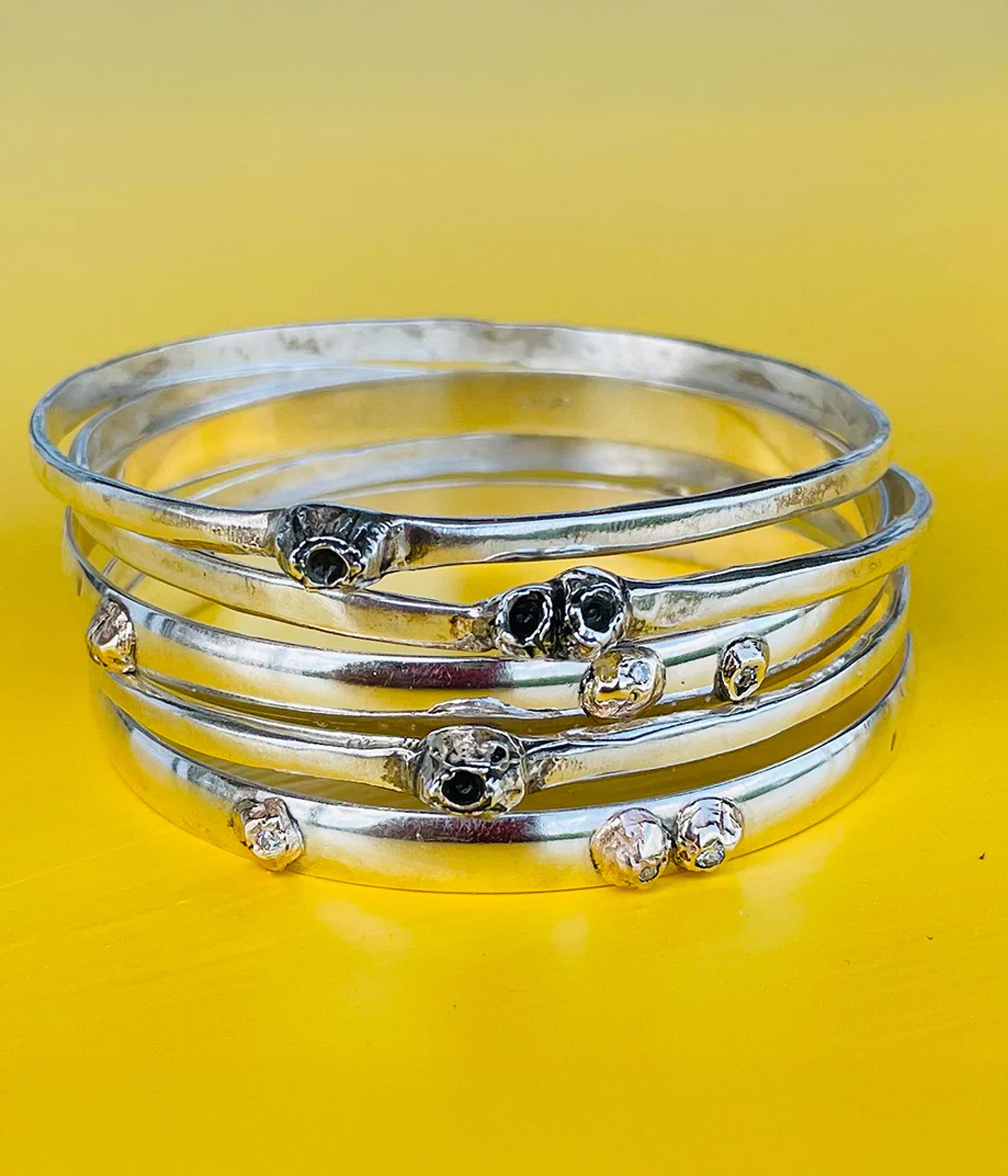 Stack of silver bangles with gemstone accents on a yellow background