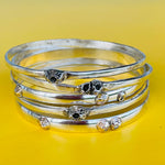 Stack of silver bangles with gemstone accents on a yellow background
