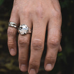 Hand wearing two silver rings with a dark background