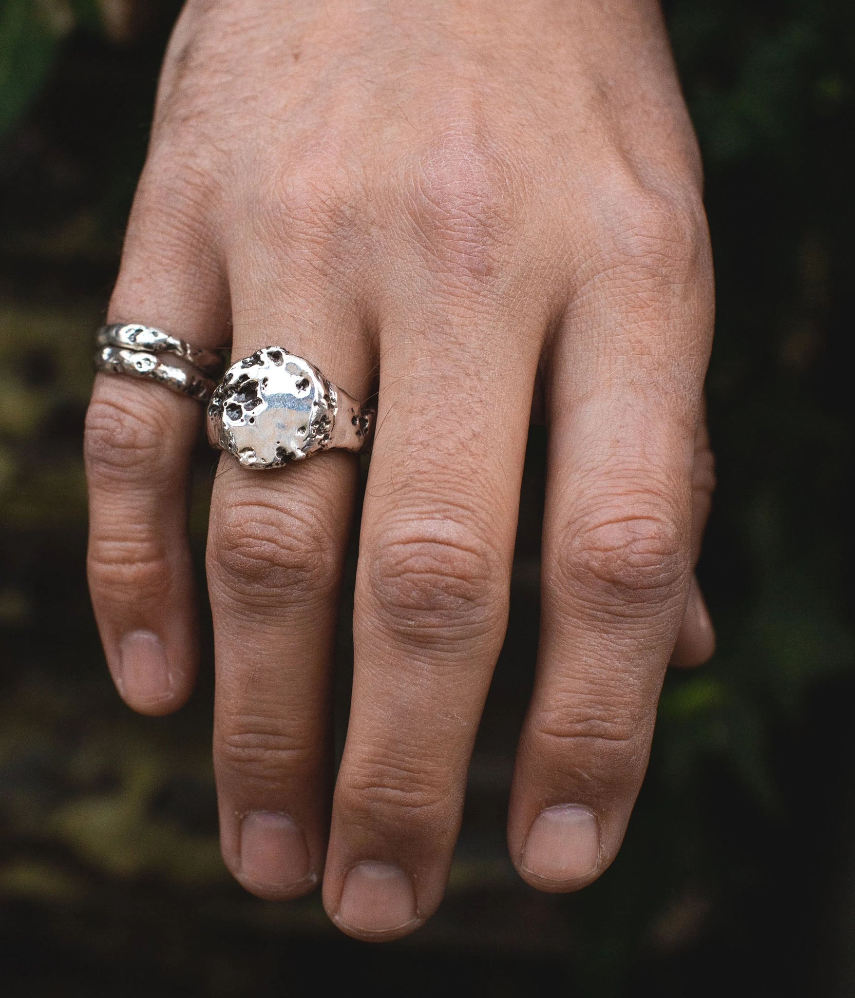 Hand wearing two silver rings with a dark background