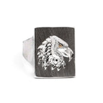 Silver ring with an eagle head design on a wooden band against a white background