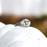 Silver ring with face design on a white stone surface