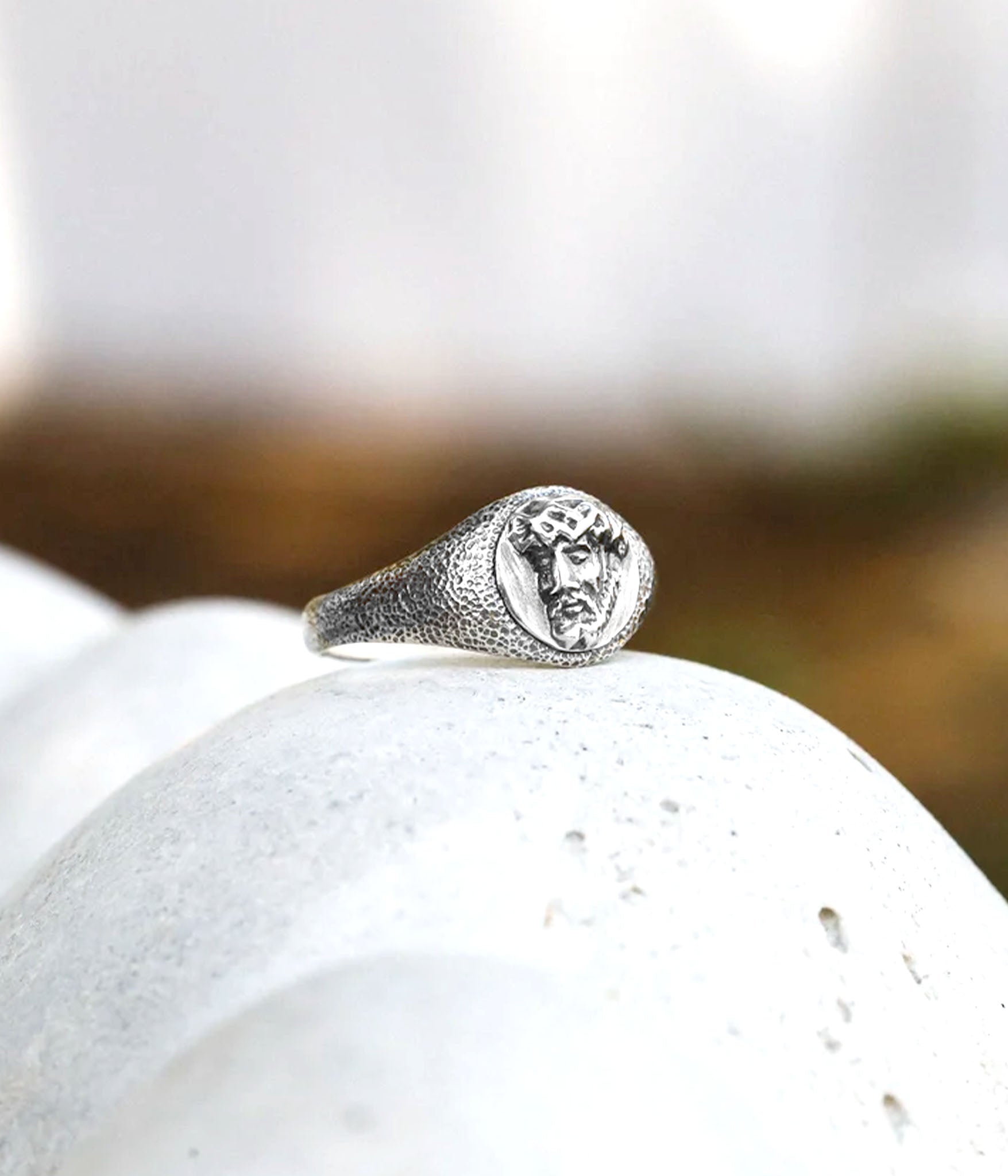 Silver ring with face design on a white stone surface