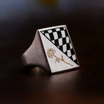Ring with checkered design and gold rose on a dark surface