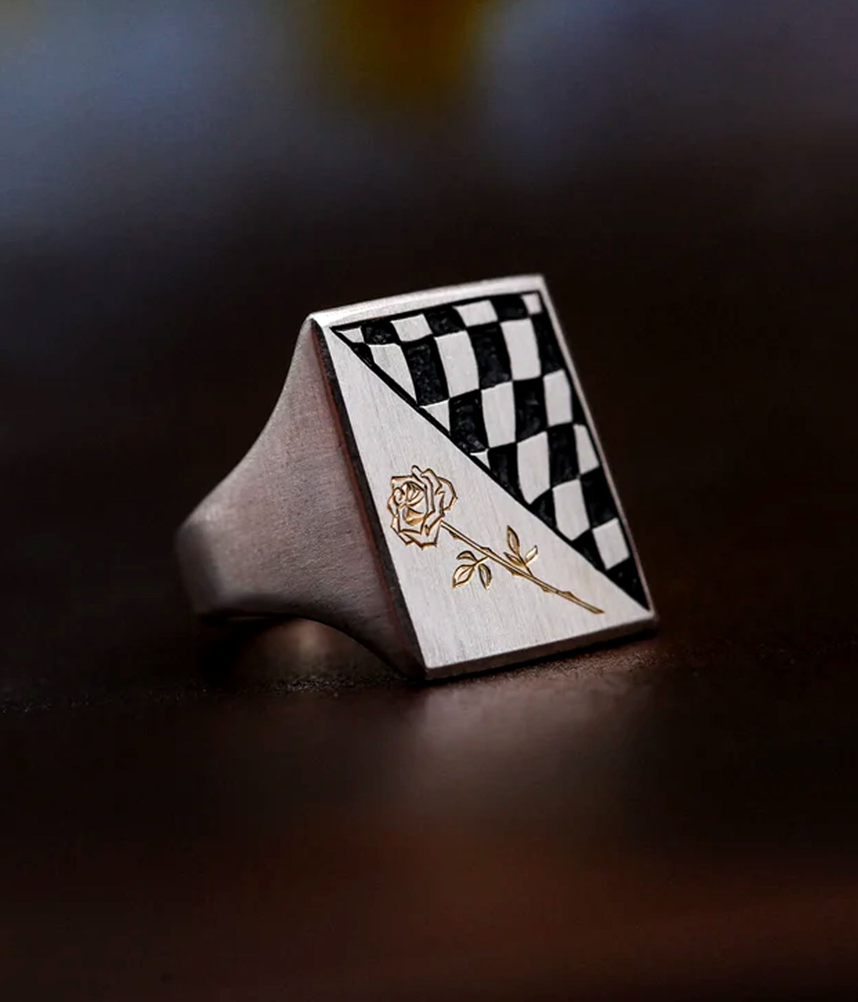 Ring with checkered design and gold rose on a dark surface