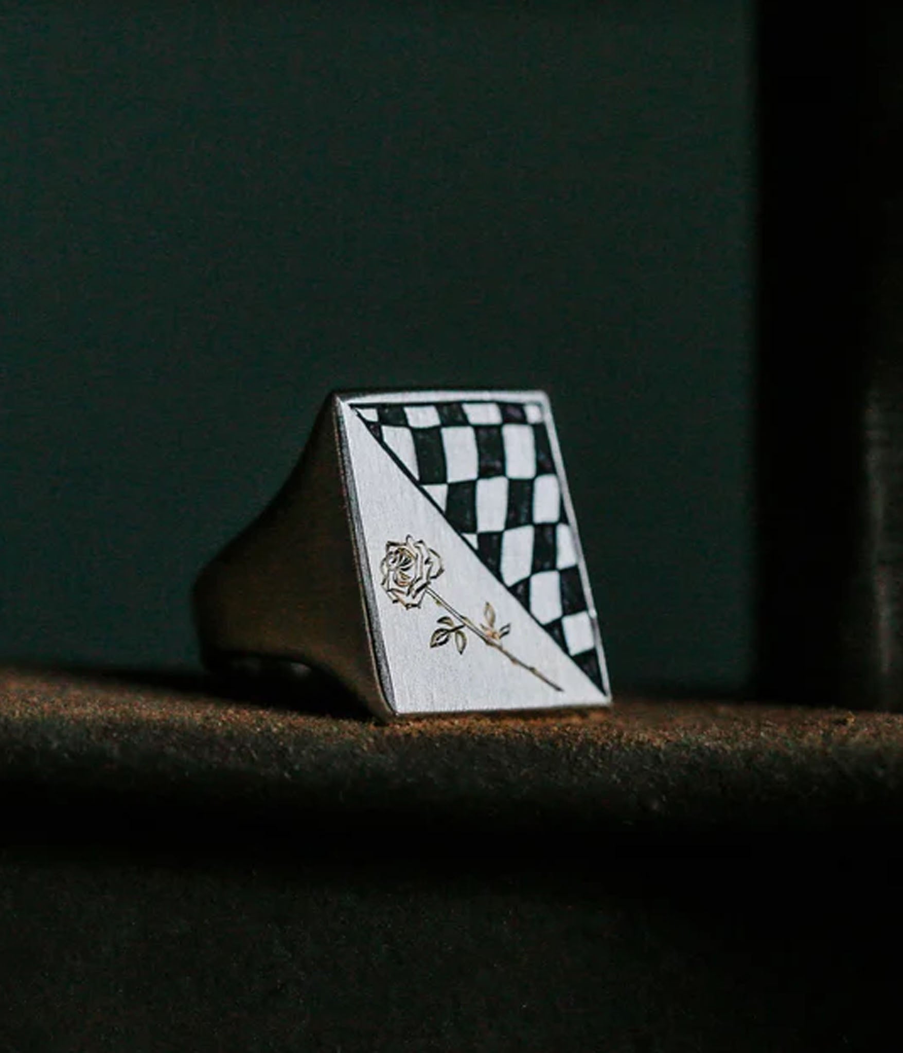 Checkered ring with a rose design on a dark surface