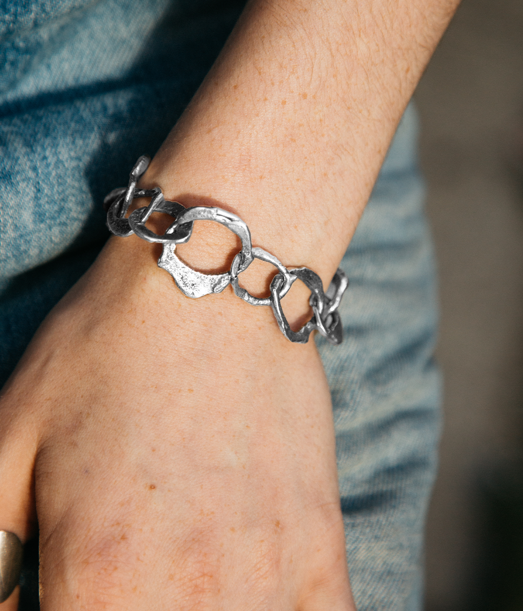 Silver chain bracelet on a wrist with a blurred denim background